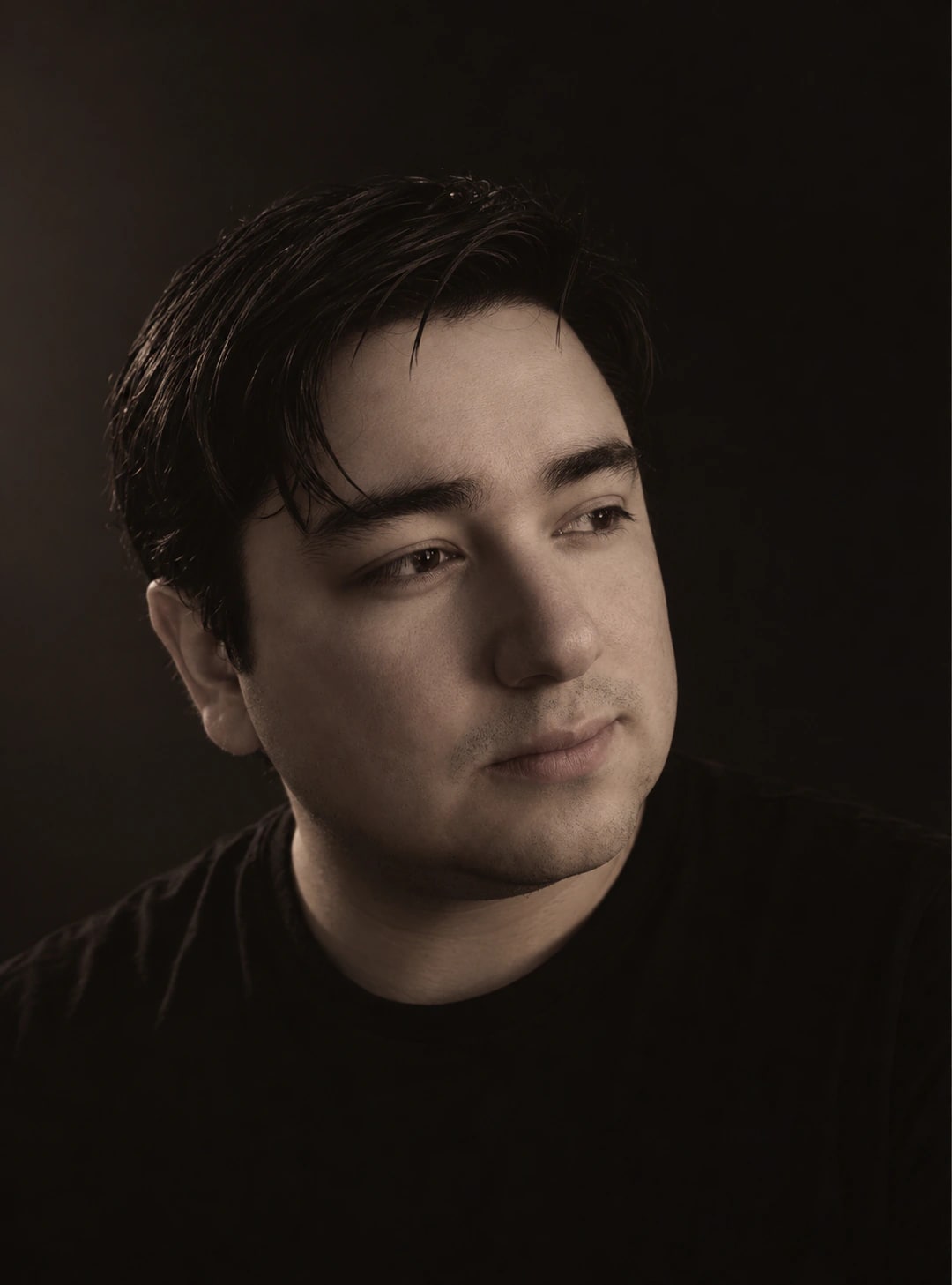 Diego Sandoval, photographed against a near-black studio background in a dark crew-neck tee, lit from one side.